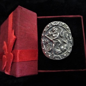 May include: A silver ring with an ornate design featuring a woman holding a staff and a dragon. The ring is in a red velvet box.