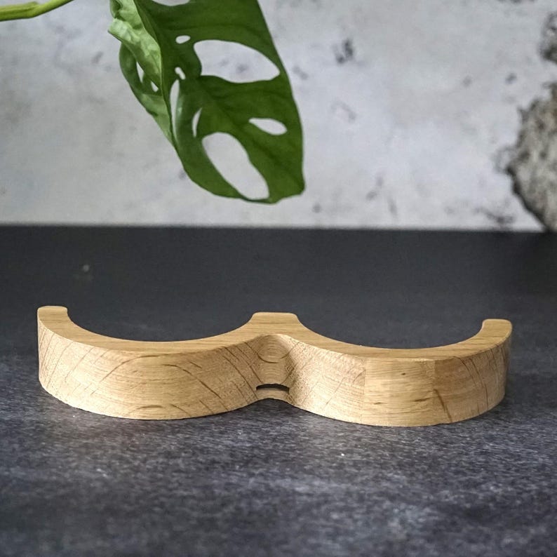May include: A light-colored wooden mustache-shaped object. The item has a curved design with a small notch in the center. The wood grain is visible. The object is likely a decorative item or a holder.