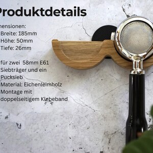 May include: A wooden espresso machine portafilter holder with a stainless steel portafilter. The holder is made of light-colored wood and is designed to hold two 58mm E61 portafilters and a puck screen. The dimensions are 185mm wide, 50mm high, and 26mm deep.
