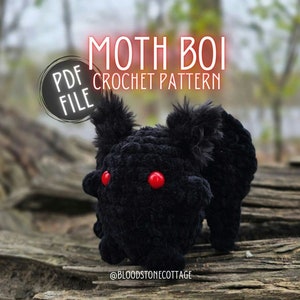 Può includere: Un giocattolo di amigurumi a forma di falena in crochet nero con occhi rossi. Il giocattolo è seduto su una superficie di legno. Il testo "MOTH BOI CROCHET PATTERN PDF FILE" è sopra il giocattolo. Il testo "@BLOODSTONECOTTAGE" è sotto il giocattolo.