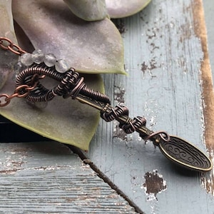 Puede incluir: Un colgante de llave envuelto en alambre de cobre con cristales transparentes y un dije de llave de bronce adornado.