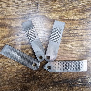 May include: Four metal files with different patterns and a hole at one end. The files are arranged in a star shape on a wooden surface.