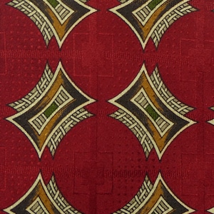 Puede incluir: Tela roja con un patrón repetido de formas de diamante marrones, beige y verdes. Los diamantes tienen un diseño tejido.