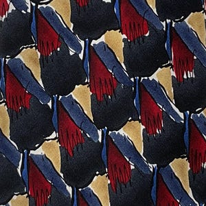 May include: A patterned necktie featuring an abstract design. The repeating pattern includes shapes in navy blue, red, tan, and blue against a white background. The tie is likely made of silk or a similar material.