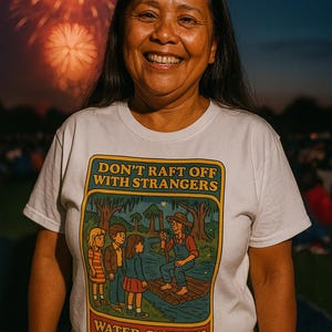 May include: A white t-shirt featuring a colourful graphic with the text "DON'T RAFT OFF WITH STRANGERS" and "WATER SAFETY". The graphic shows a cartoon scene of children and a man on a raft. Fireworks are visible in the background.