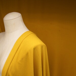 May include: A close-up of a yellow fabric draped over a dress form. The fabric is smooth and has a slight sheen.