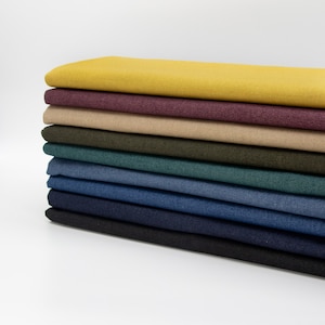 May include: A stack of fabric swatches in various colours, including mustard yellow, burgundy, beige, dark green, teal, denim blue, navy blue, and black.