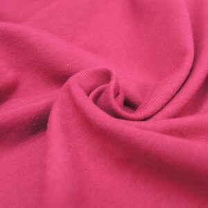 Puede incluir: Primer plano de una tela suave de color rojo con una textura lisa. La tela est&aacute; doblada y drapeada, creando un aspecto fluido y elegante.