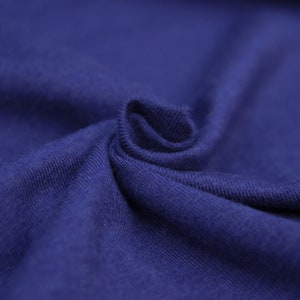 May include: Close-up of a soft, blue fabric with a textured surface. The fabric is folded and draped, showing its smooth texture.