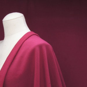 Puede incluir: Primer plano de una tela de color rojo carmes&iacute; oscuro drapeada sobre un maniqu&iacute; blanco. La tela tiene una textura suave y lisa.