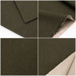 May include: Close-up of a dark green canvas fabric with a subtle texture. The fabric is folded over, revealing a beige underside.