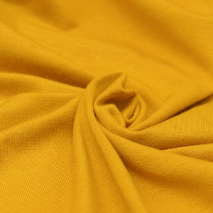 May include: Close-up of a soft, yellow fabric with a ribbed texture. The fabric is folded and draped, creating a smooth, flowing look.