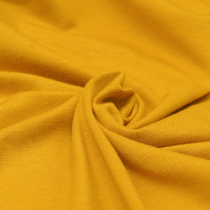 May include: Close-up of a soft, yellow fabric with a ribbed texture. The fabric is folded and draped, creating a smooth, flowing look.
