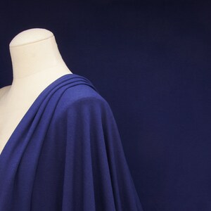May include: A close-up of a blue fabric draped over a white dress form. The fabric is soft and flowing, with a subtle sheen.