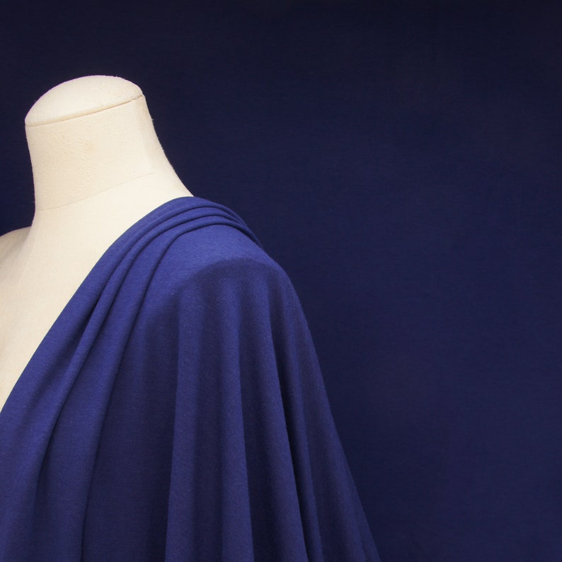 May include: A close-up of a blue fabric draped over a white dress form. The fabric is soft and flowing, with a subtle sheen.