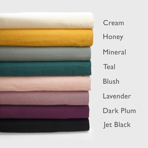 Puede incluir: Una pila de telas plegadas en varios colores: crema, miel, mineral, verde azulado, rubor, lavanda, ciruela oscura y negro azabache. Los nombres de los colores se muestran a la derecha.