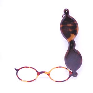 May include: A vintage pair of tortoiseshell eyeglasses with a matching handle. The glasses have round lenses and a patterned frame in shades of brown and yellow. The handle is elongated with a similar pattern.