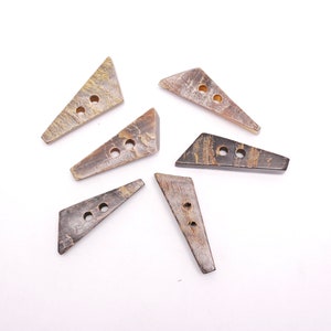 Peut inclure: Six boutons triangulaires brun et noir avec deux trous chacun. Les boutons sont faits d'un matériau naturel, peut-être de la corne ou de l'os.