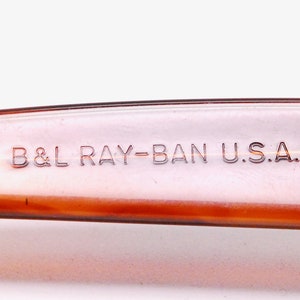 Puede incluir: Primer plano del brazo de pl&aacute;stico marr&oacute;n de unas gafas de sol Ray-Ban. El texto "B&L RAY-BAN U.S.A." est&aacute; grabado en relieve en el brazo.