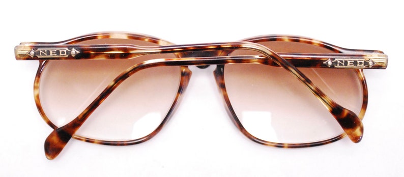 May include: Tortoiseshell eyeglasses with gold accents and the word "NEO" on each arm.