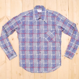 Może przedstawiać: Koszula w długim rękawem w niebiesko-białą kratę z czerwonymi akcentami. Koszula ma kołnierzyk zapinany na guziki i kieszeń na lewej piersi.