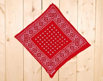 Pode incluir: Bandana vermelha com um padrão paisley branco e uma borda branca. A bandana está pendurada em uma parede de madeira.