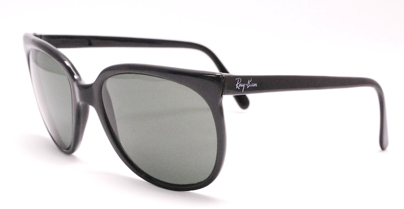 以下が含まれることがあります： 緑色のレンズが付いた黒いレイバンサングラス。サングラスはクラシックな角張った形と薄いフレームをしています。