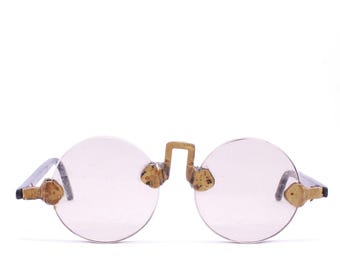 May include: A pair of round, pink-tinted spectacles with gold-coloured metal accents and a silver metal frame.
