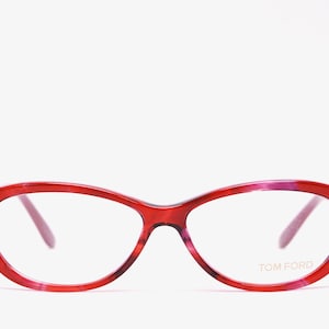 May include: Red and pink cat-eye glasses with clear lenses and the brand name "TOM FORD" printed on the right lens.