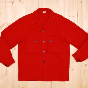 May include: A red long-sleeved shirt with a button-up front and two flap pockets. The shirt has a classic collar and is made of a soft, warm fabric.