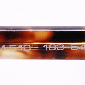 May include: Close-up of the inside of a tortoiseshell-patterned eyeglass frame with the text "FORUM 510 - 183 - 54□18 140" printed in white.