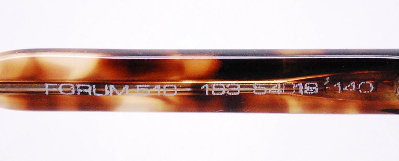 May include: Close-up of the inside of a tortoiseshell-patterned eyeglass frame with the text "FORUM 510 - 183 - 54□18 140" printed in white.