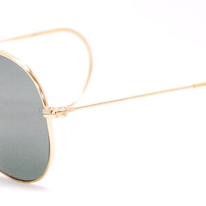 Pode incluir: &Oacute;culos de sol aviador dourados com lentes verdes e uma barra de sobrancelha de couro marrom.