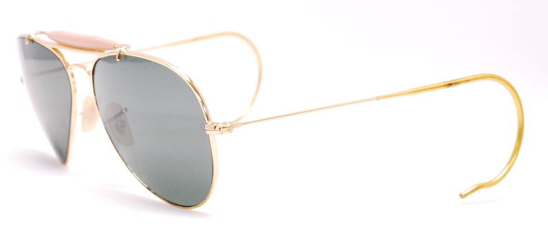 Pode incluir: &Oacute;culos de sol aviador dourados com lentes verdes e uma barra de sobrancelha de couro marrom.