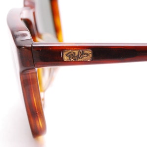 May include: Close-up of the side of a pair of tortoiseshell Ray-Ban sunglasses. The Ray-Ban logo is visible on the side of the frame.