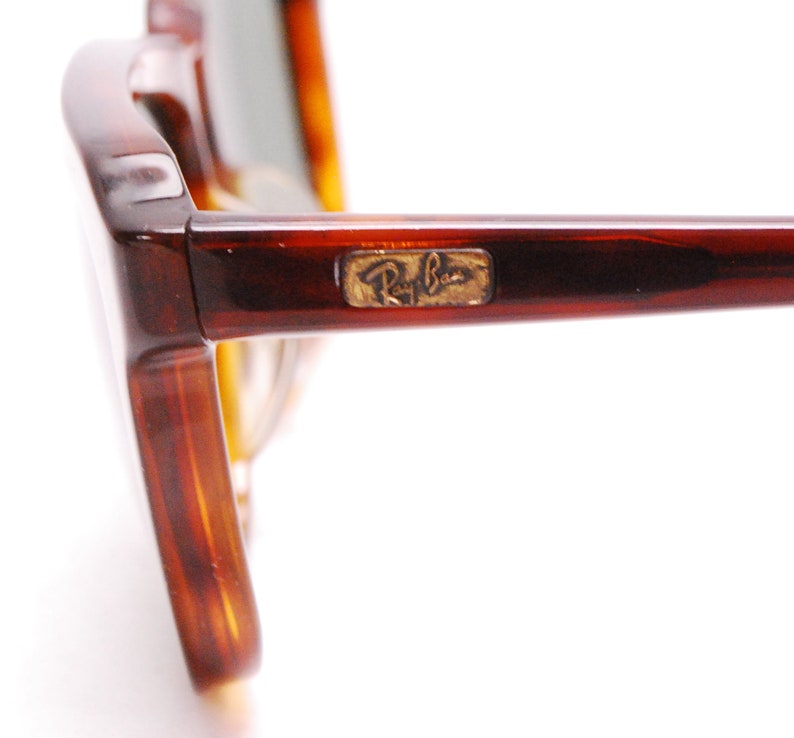 May include: Close-up of the side of a pair of tortoiseshell Ray-Ban sunglasses. The Ray-Ban logo is visible on the side of the frame.
