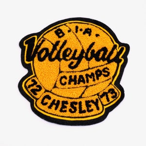 以下が含まれることがあります： バレーボールと「Volleyball Champs '72 Chesley '73」という文字が刺繍された黒と黄色のパッチです。