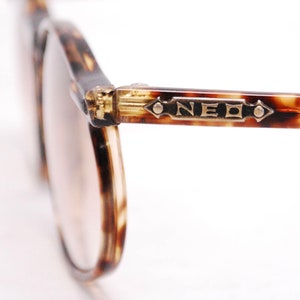 May include: Close-up of tortoiseshell eyeglasses with gold accents and the word "NEO" on the frame.