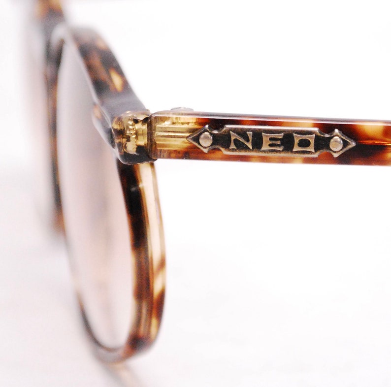 May include: Close-up of tortoiseshell eyeglasses with gold accents and the word "NEO" on the frame.