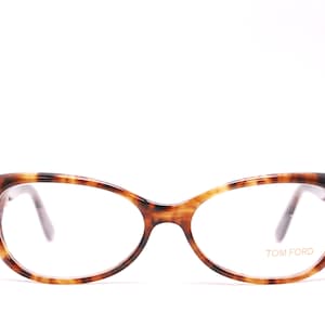 May include: Tortoise shell eyeglasses with a cat-eye frame and clear lenses. The brand name "TOM FORD" is printed on the right lens.