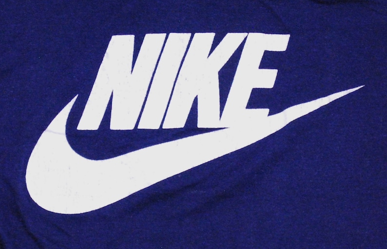 Puede incluir: Logotipo blanco de Nike con la palabra "NIKE" en una fuente blanca en negrita sobre un fondo azul oscuro.