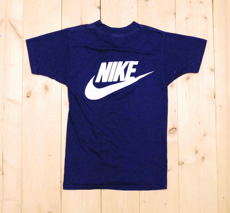 Puede incluir: Una camiseta azul marino con un logotipo blanco de Nike en forma de swoosh en la espalda.