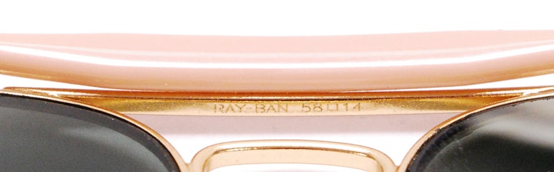 Pode incluir: Close-up da arma&ccedil;&atilde;o de metal dourado de um par de &oacute;culos de sol Ray-Ban. A arma&ccedil;&atilde;o tem o texto "RAY-BAN 58 114" gravado.