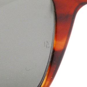 Puede incluir: Primer plano del marco de carey de unas gafas de sol. El marco tiene un patr&oacute;n marr&oacute;n y &aacute;mbar. La lente es gris y tiene el n&uacute;mero "13" grabado.