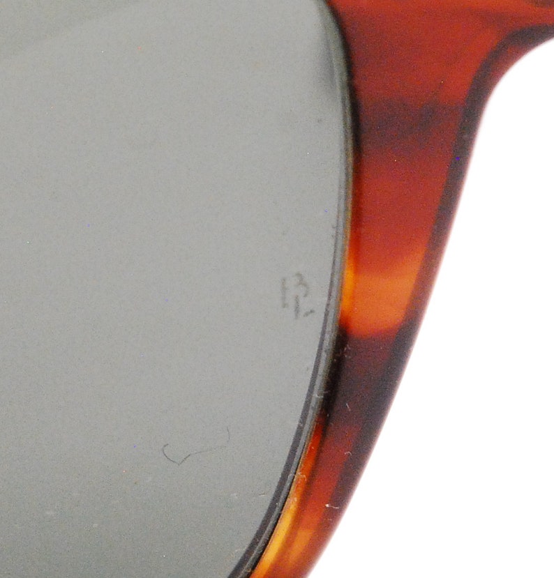 Puede incluir: Primer plano del marco de carey de unas gafas de sol. El marco tiene un patr&oacute;n marr&oacute;n y &aacute;mbar. La lente es gris y tiene el n&uacute;mero "13" grabado.