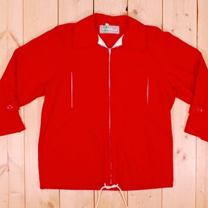 May include: A red zip-up jacket with a white collar and white trim. The jacket has a drawstring at the bottom and a label that says "Bella" on the left side of the collar.