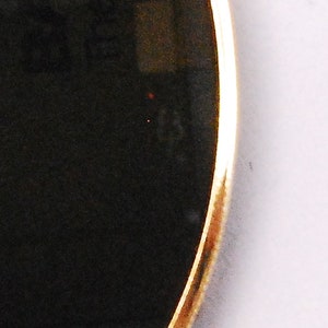 May include: A round sunglasses lens with a gold rim and a black tint.