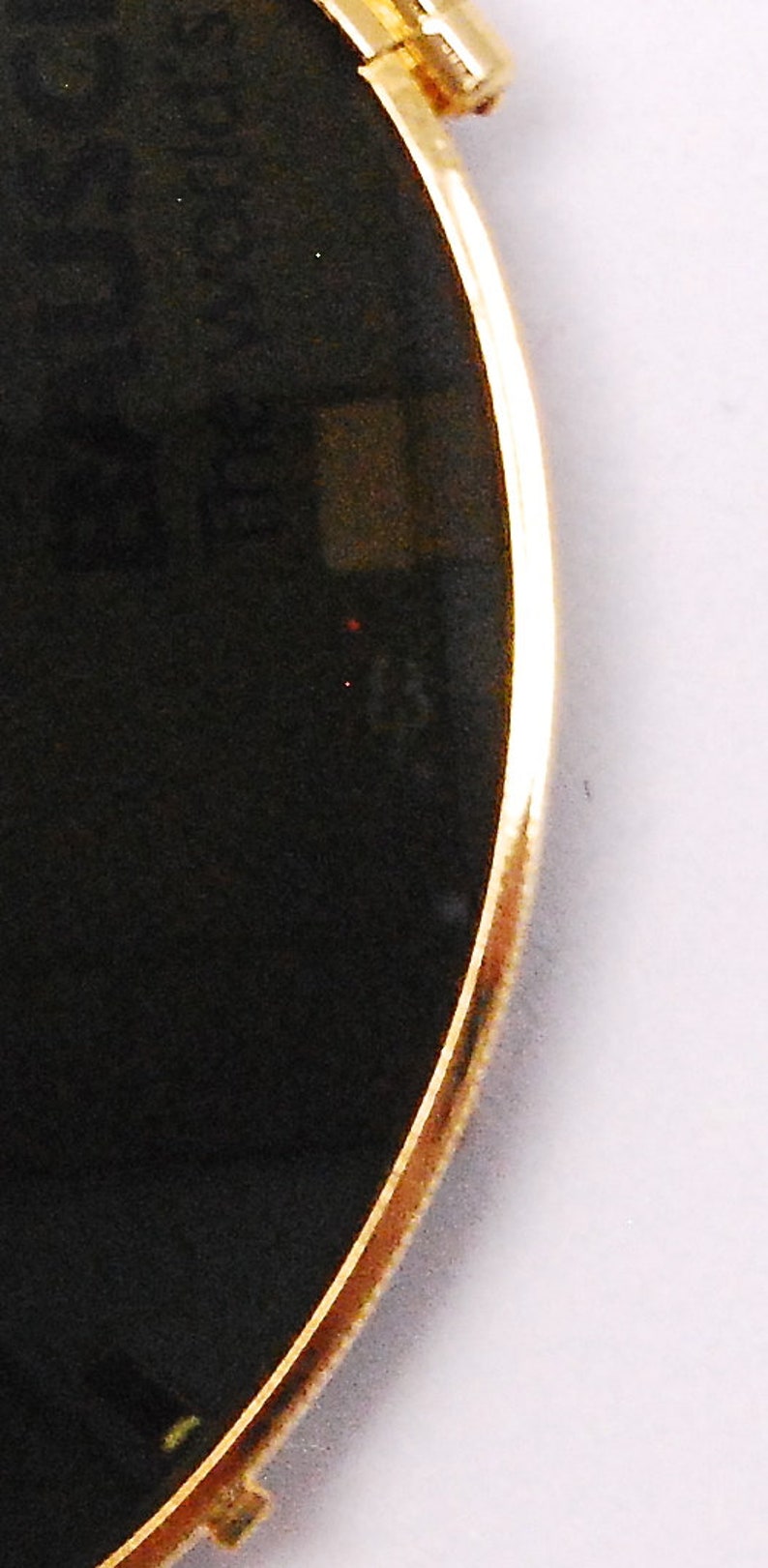 May include: A round sunglasses lens with a gold rim and a black tint.