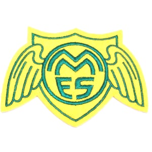 Può includere: Toppa ricamata gialla con uno scudo e ali verdi. Lo scudo ha un cerchio con le lettere "M.E.S." al suo interno.