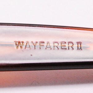 Puede incluir: Primer plano de la inscripci&oacute;n "WAYFARER II" en un marco de pl&aacute;stico marr&oacute;n.